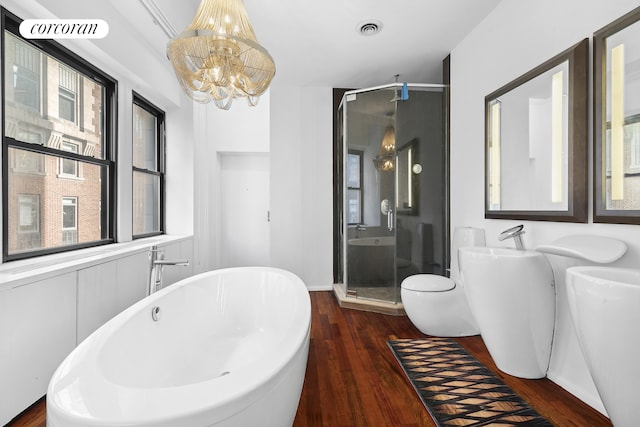 bathroom featuring wood finished floors, visible vents, an inviting chandelier, a freestanding tub, and a stall shower