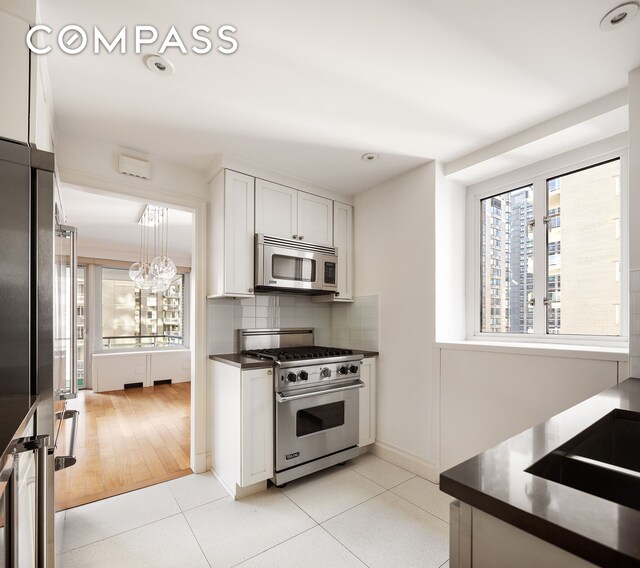 200 E 66th St Unit D1203, New York City, NY 10065 - kitchen featuring light tile patterned flooring, stainless steel appliances, decorative backsplash, white cabinets, and dark countertops