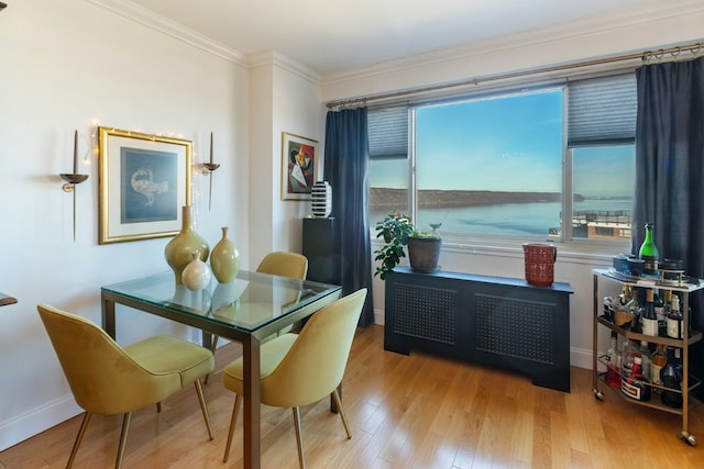 dining room with radiator, crown molding, light wood-style flooring, and baseboards