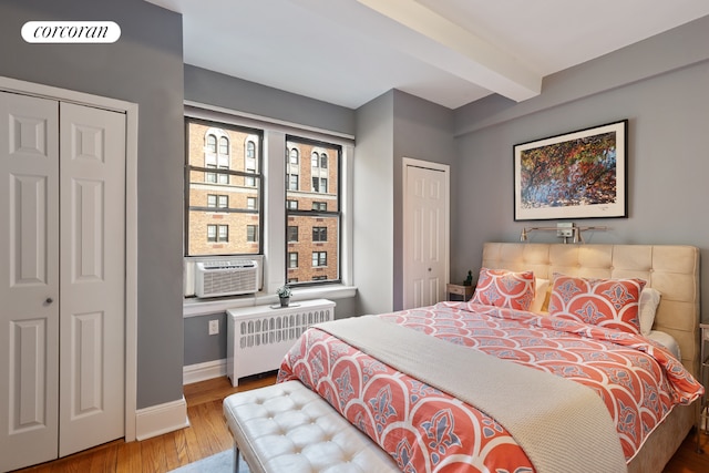 bedroom featuring radiator, beamed ceiling, hardwood / wood-style flooring, and two closets