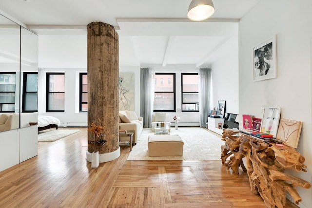 living room with baseboard heating, ornate columns, beam ceiling, and light wood-type flooring