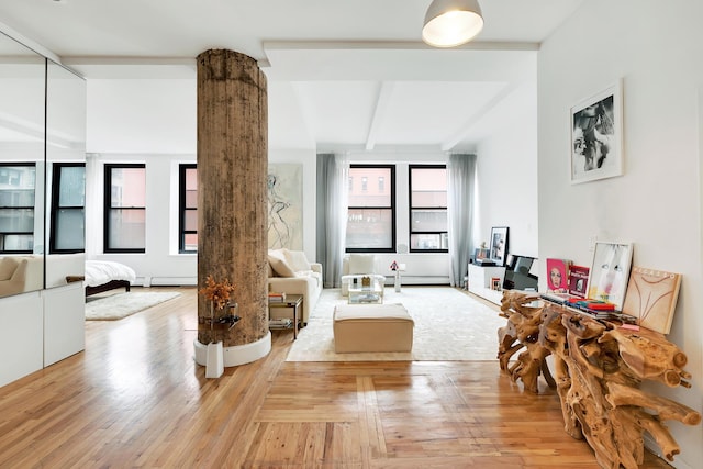 living area featuring a baseboard heating unit, beam ceiling, light wood-style floors, and decorative columns