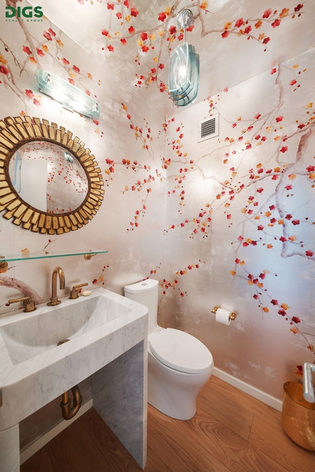 half bath featuring toilet, wood finished floors, visible vents, and baseboards