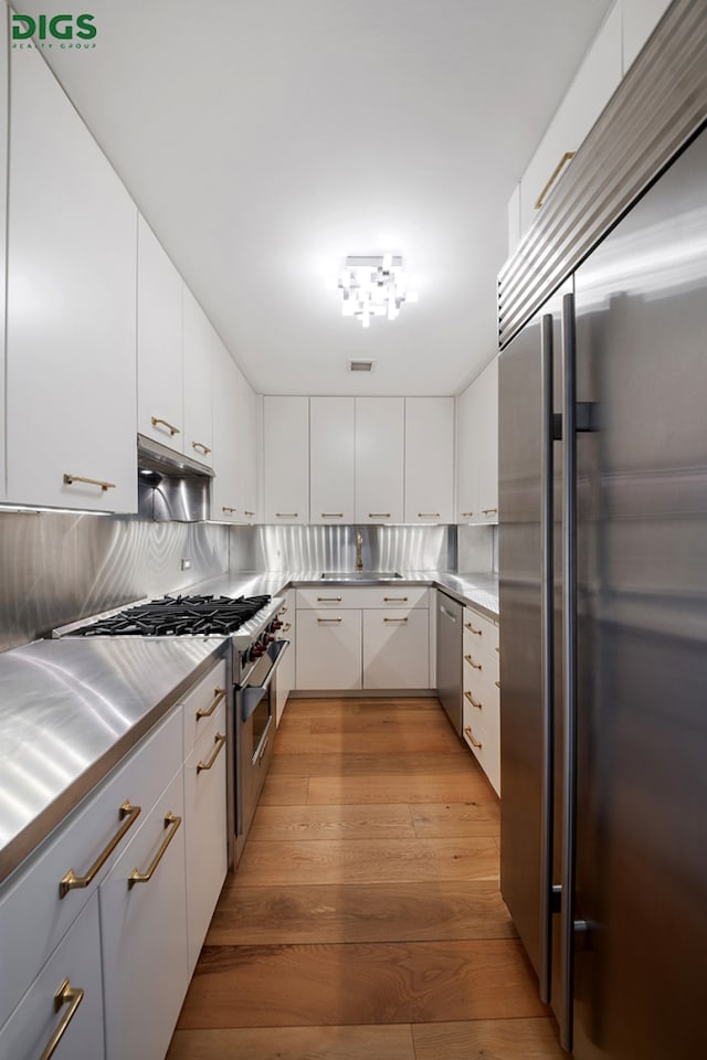 kitchen with stainless steel countertops, high quality appliances, wood finished floors, and white cabinetry