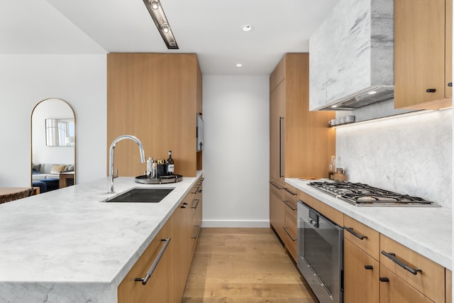 kitchen featuring custom exhaust hood, wall oven, backsplash, light hardwood / wood-style flooring, and sink