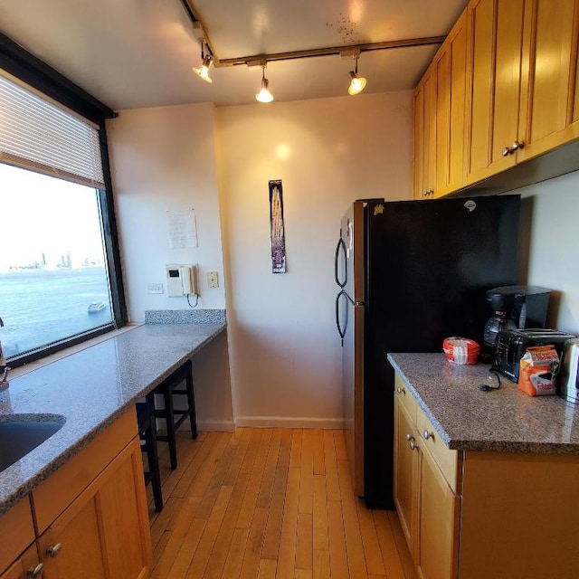 kitchen featuring stone countertops, a sink, baseboards, light wood-style floors, and freestanding refrigerator