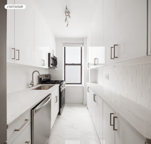 kitchen featuring white cabinetry, stainless steel appliances, tasteful backsplash, light stone countertops, and sink