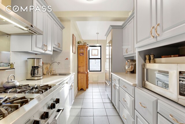 kitchen featuring extractor fan, sink, backsplash, hanging light fixtures, and light tile patterned flooring