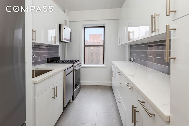 99-21 67th Rd Unit 7A, New York City, NY 11375 - kitchen featuring stainless steel appliances, baseboards, decorative backsplash, white cabinetry, and light stone counters
