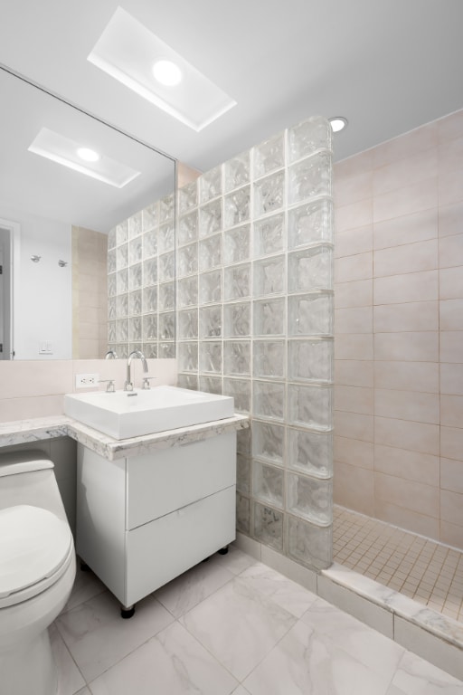 bathroom featuring walk in shower, vanity, tile walls, and toilet