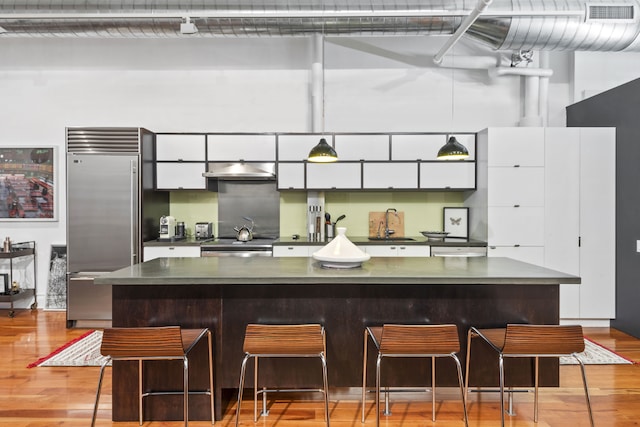 kitchen with white cabinetry, stainless steel appliances, a breakfast bar, and light hardwood / wood-style flooring