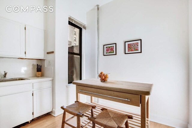 kitchen featuring white appliances, a sink, white cabinetry, light countertops, and wood finished floors