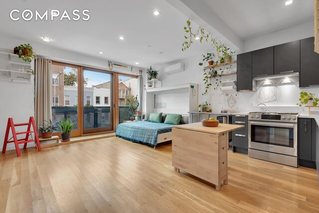 kitchen featuring tasteful backsplash, dark cabinetry, a wall unit AC, light wood-style floors, and stainless steel electric range oven