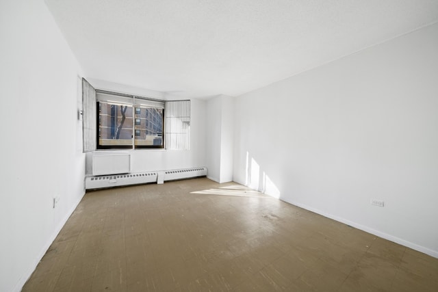 spare room featuring a baseboard heating unit, tile patterned floors, and baseboards