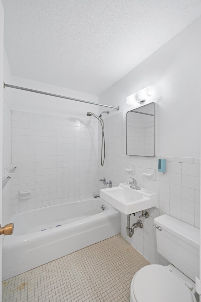 full bathroom with a textured ceiling, tile patterned flooring, toilet, tile walls, and washtub / shower combination