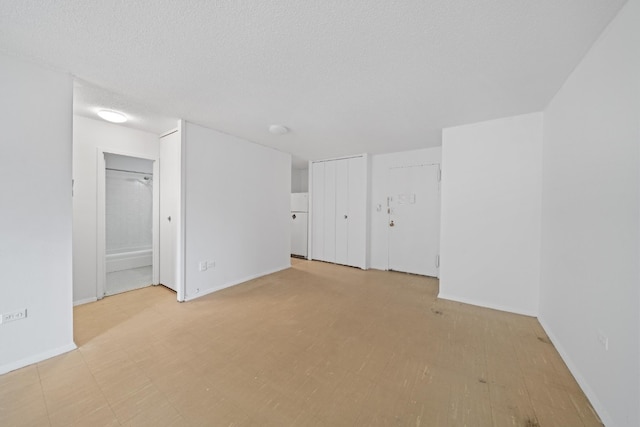 empty room with light floors, baseboards, and a textured ceiling