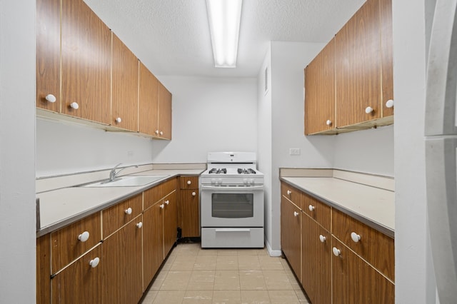 kitchen featuring a textured ceiling, white gas stove, a sink, light countertops, and brown cabinets