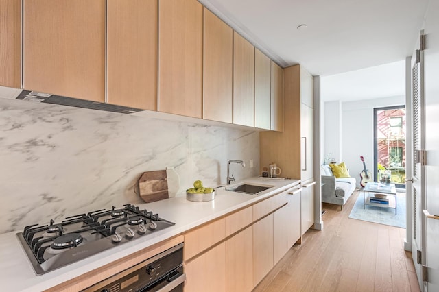 kitchen with stainless steel gas cooktop, light countertops, backsplash, light wood-style floors, and a sink