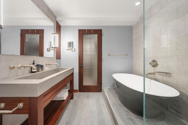 bathroom with wood finished floors, a soaking tub, backsplash, and vanity