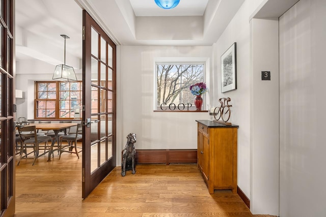 interior space featuring light wood finished floors, french doors, baseboards, and a raised ceiling