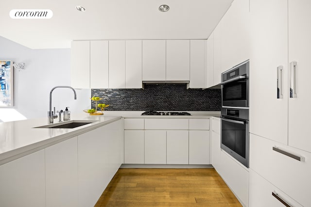 kitchen featuring double oven, black stovetop, white cabinets, a sink, and backsplash