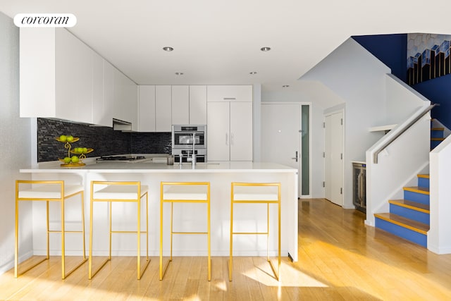 kitchen with backsplash, light hardwood / wood-style floors, kitchen peninsula, a kitchen breakfast bar, and white cabinets