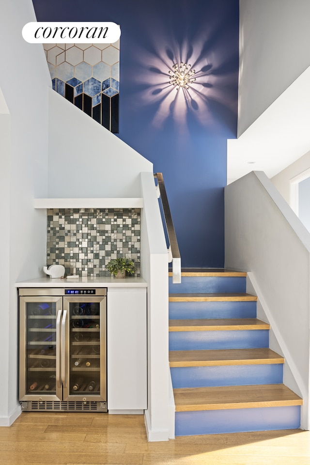 staircase with beverage cooler, wood finished floors, and a bar