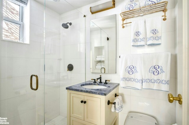 bathroom featuring vanity, toilet, tile walls, and a shower with shower door