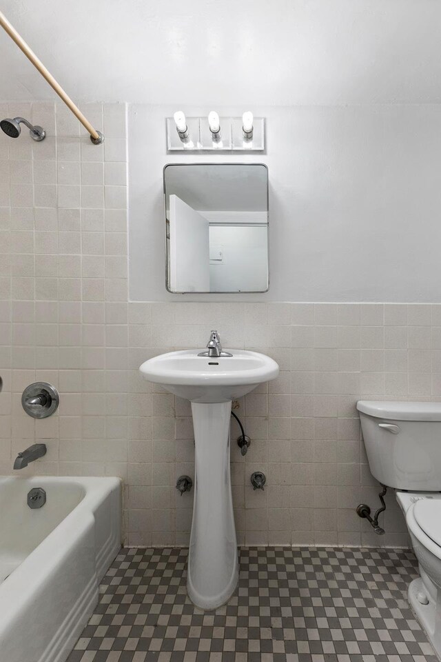 bathroom featuring shower / bathing tub combination, toilet, tile walls, and wainscoting