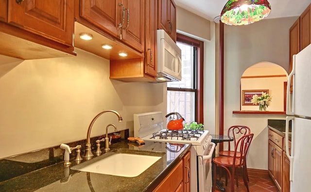 kitchen with sink, dark stone countertops, dark tile patterned floors, and white appliances