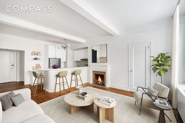 living area featuring a fireplace with flush hearth, beamed ceiling, wood finished floors, and a notable chandelier