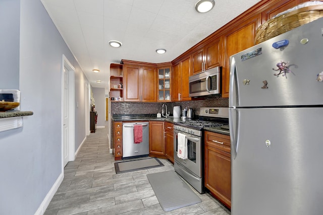 kitchen with brown cabinetry, dark countertops, a sink, appliances with stainless steel finishes, and backsplash