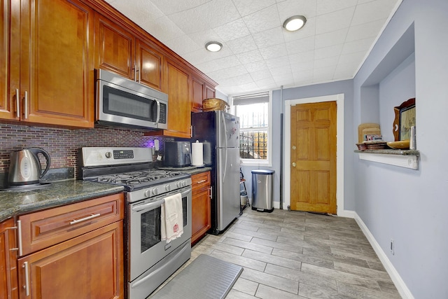 kitchen featuring brown cabinetry, baseboards, light wood-type flooring, appliances with stainless steel finishes, and backsplash