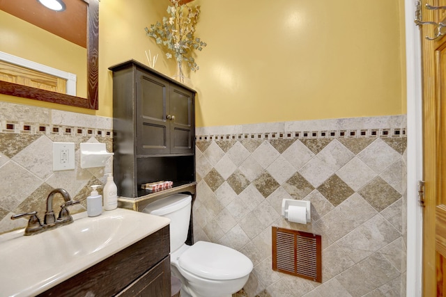half bath featuring wainscoting, vanity, toilet, tile walls, and visible vents
