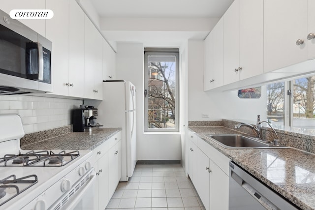 kitchen featuring light tile patterned floors, backsplash, appliances with stainless steel finishes, white cabinets, and a sink