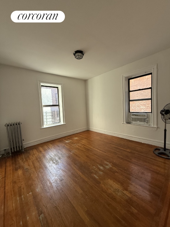 empty room with radiator heating unit, dark hardwood / wood-style flooring, and cooling unit