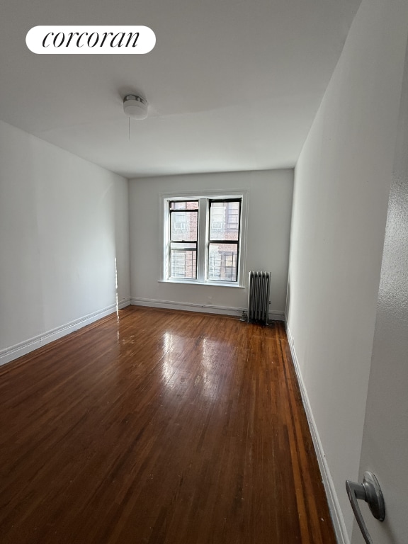 unfurnished room with radiator and dark wood-type flooring