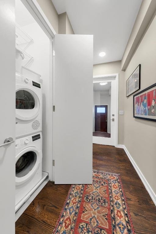 laundry room featuring stacked washing maching and dryer and dark hardwood / wood-style flooring