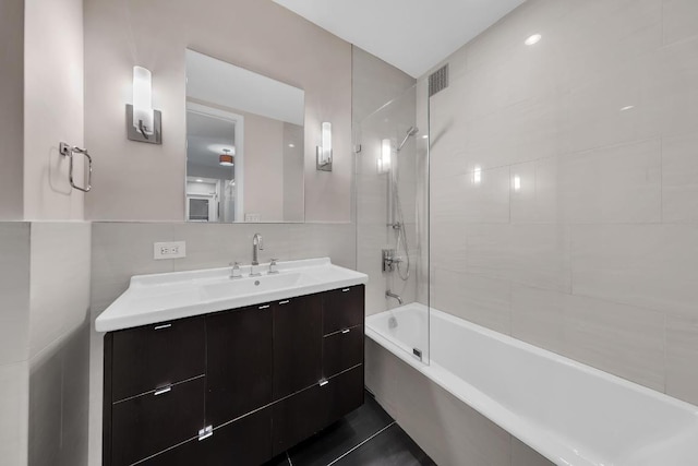 bathroom featuring tile patterned flooring, tiled shower / bath, tile walls, and vanity