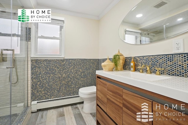 bathroom featuring toilet, vanity, a baseboard heating unit, ornamental molding, and a shower with door