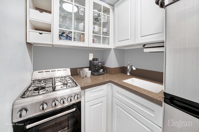 kitchen with a sink, white cabinets, glass insert cabinets, appliances with stainless steel finishes, and dark countertops