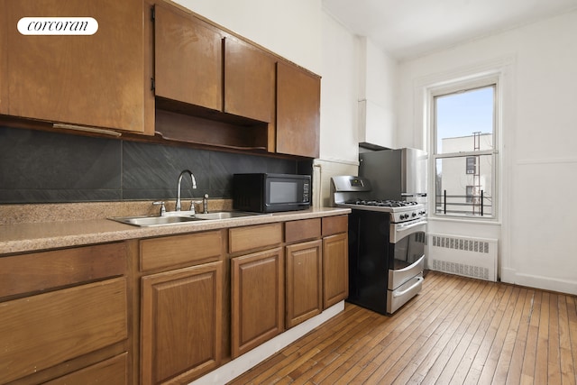 kitchen featuring stainless steel gas range oven, radiator, light wood-type flooring, black microwave, and a sink