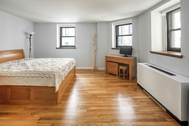 bedroom featuring radiator heating unit, light wood-style flooring, and baseboards