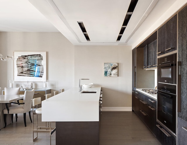 kitchen featuring a sink, a breakfast bar, dark wood finished floors, and dark brown cabinetry
