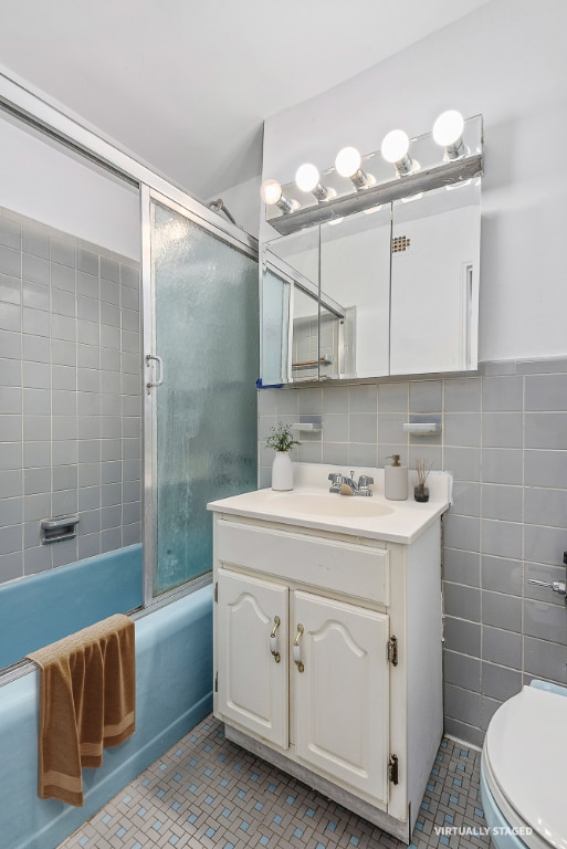 full bathroom featuring toilet, vanity, tile walls, combined bath / shower with glass door, and decorative backsplash