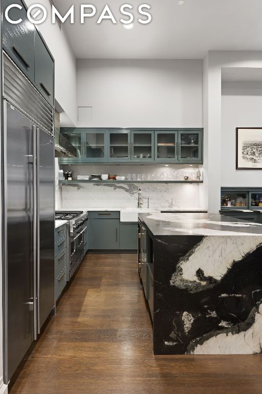 kitchen featuring premium appliances, decorative backsplash, dark hardwood / wood-style flooring, wall chimney exhaust hood, and sink