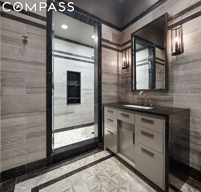 bathroom with a tile shower, vanity, and tile walls