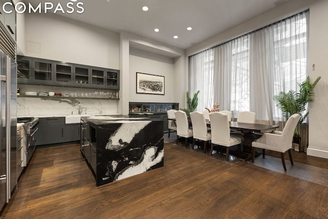 interior space with backsplash, a kitchen island, sink, high end stainless steel range, and dark hardwood / wood-style flooring