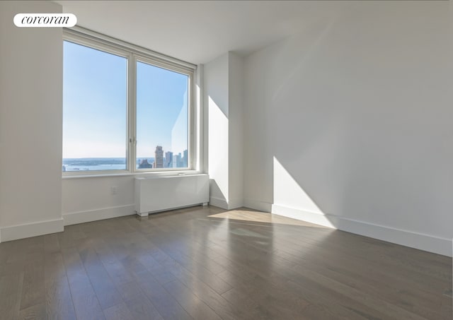 empty room featuring baseboards, a water view, wood finished floors, and radiator