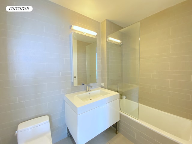 bathroom featuring tiled shower / bath, toilet, vanity, and tile walls